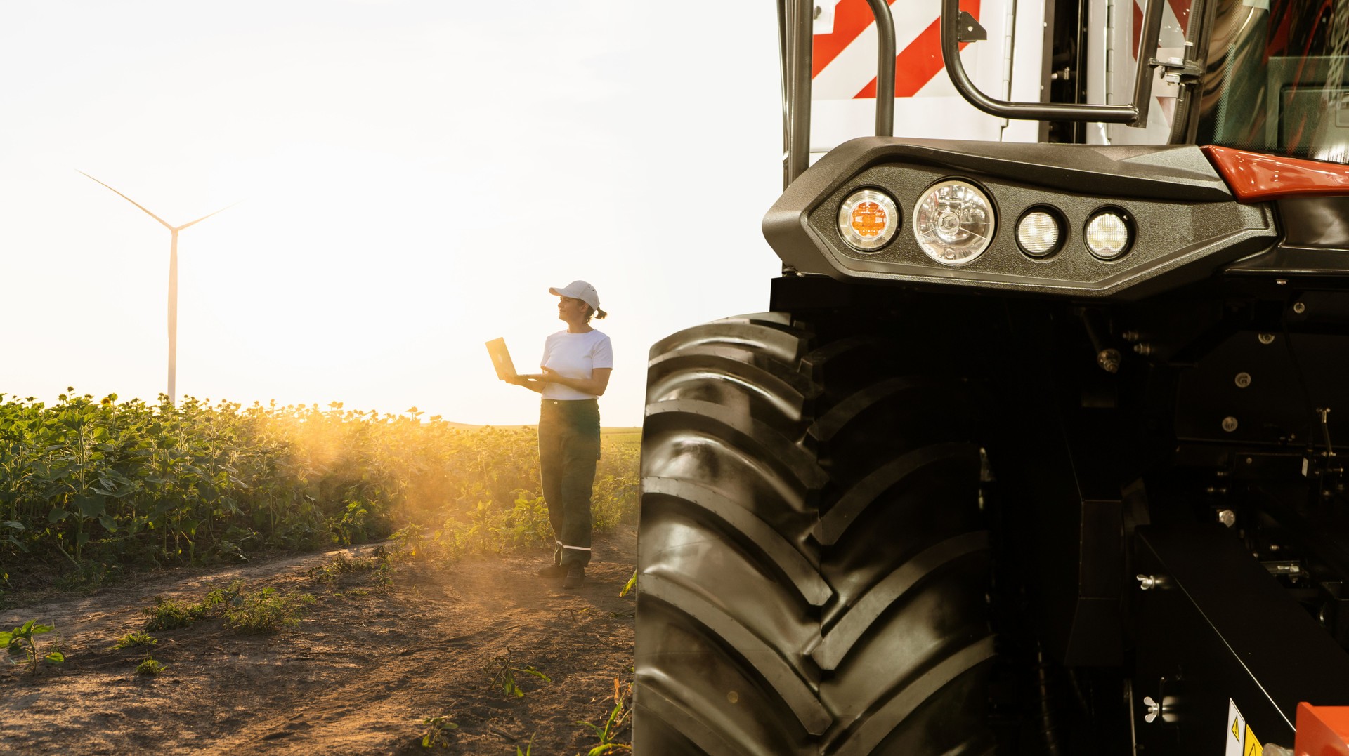 Female farmer with laptop stands near combine harvester. Smart farming concept.